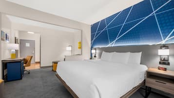 Habitación de hotel con una cama grande, un escritorio, una silla, una mesita de noche y un televisor montado en la pared.