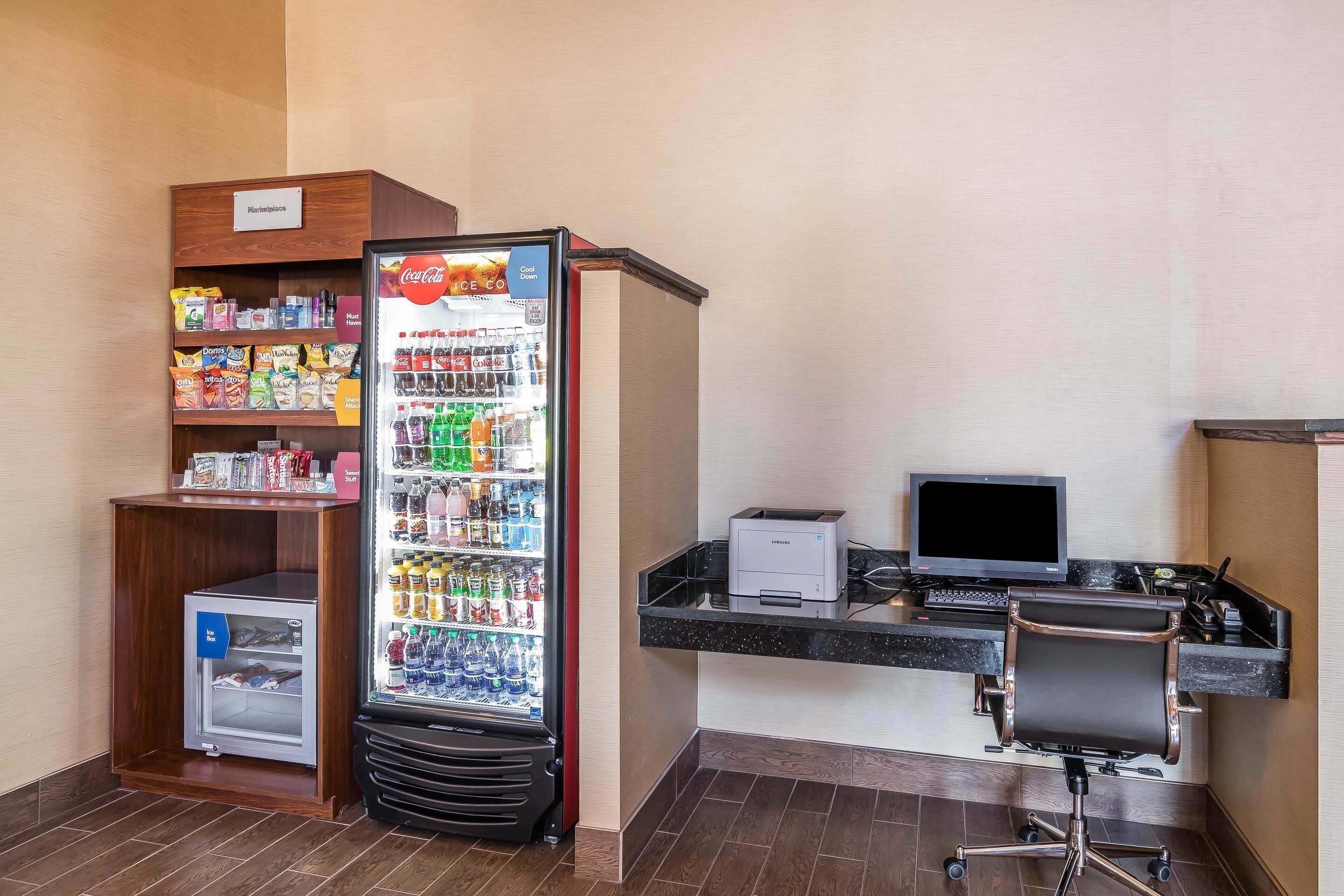 A hotel room with a minibar, a refrigerator stocked with beverages, a desk with a computer, and a chair.