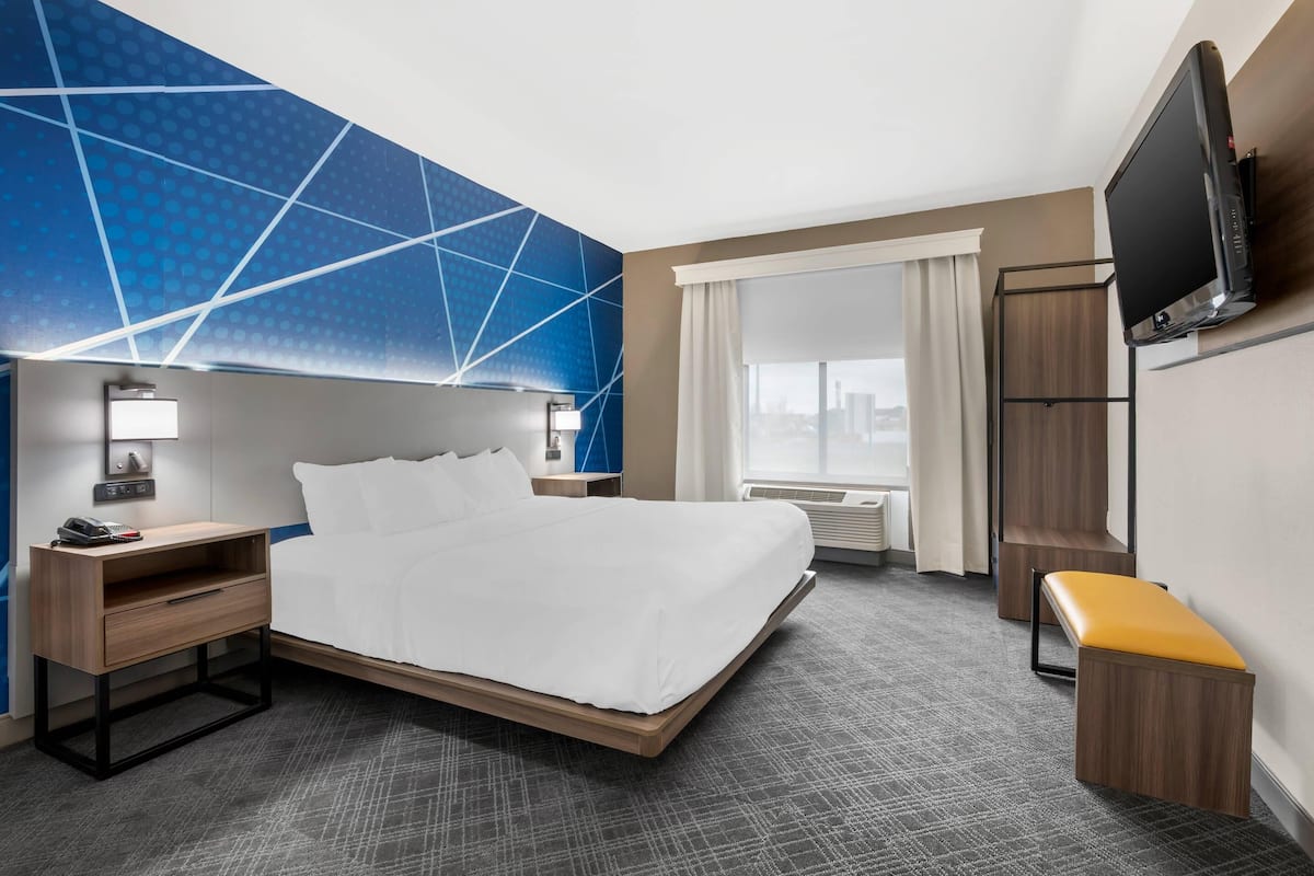 A hotel room with a bed, bedside tables, a TV, a bench, and a city view.