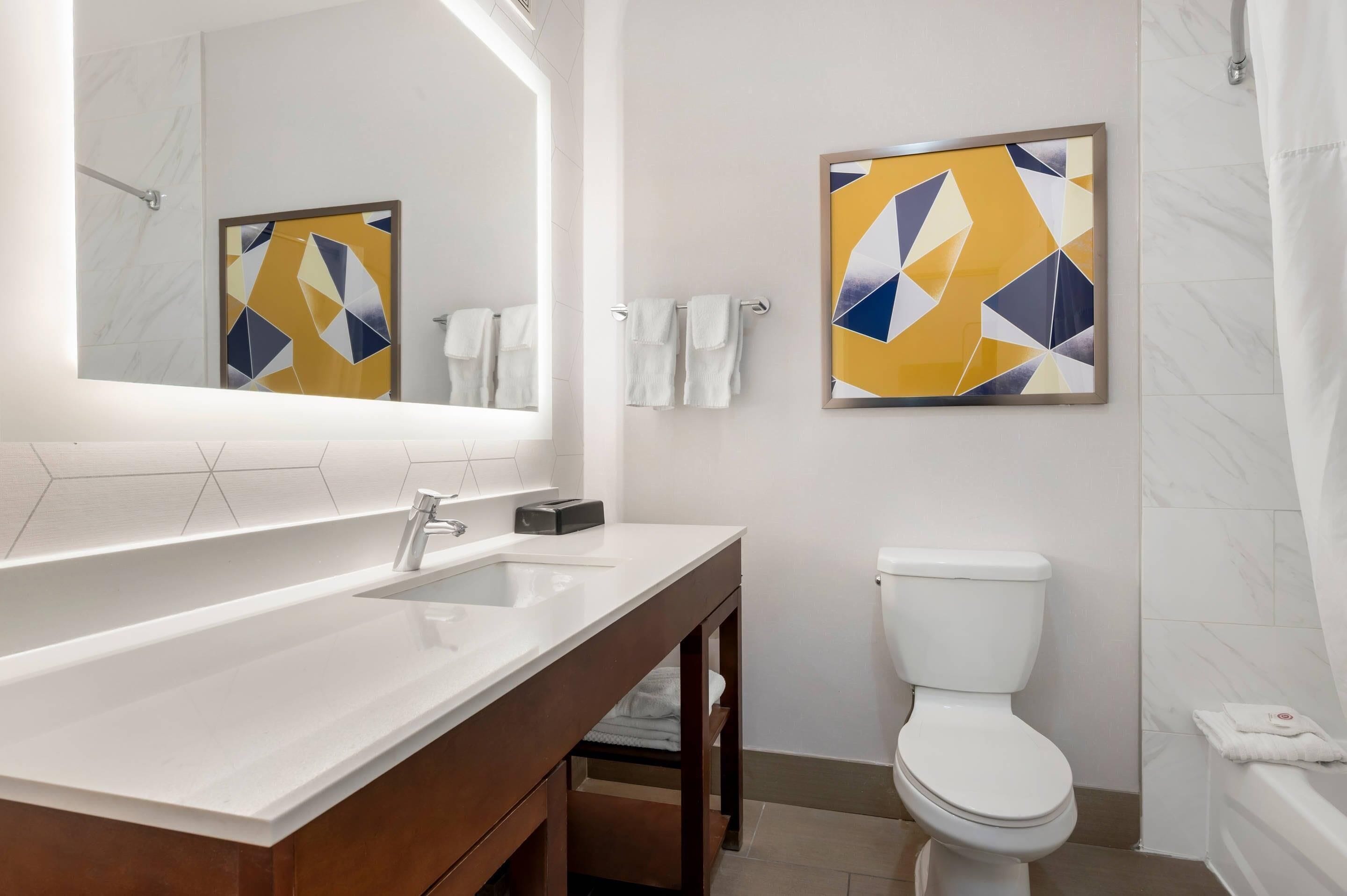 A modern bathroom with a large mirror, a white sink, a toilet, and a bathtub.