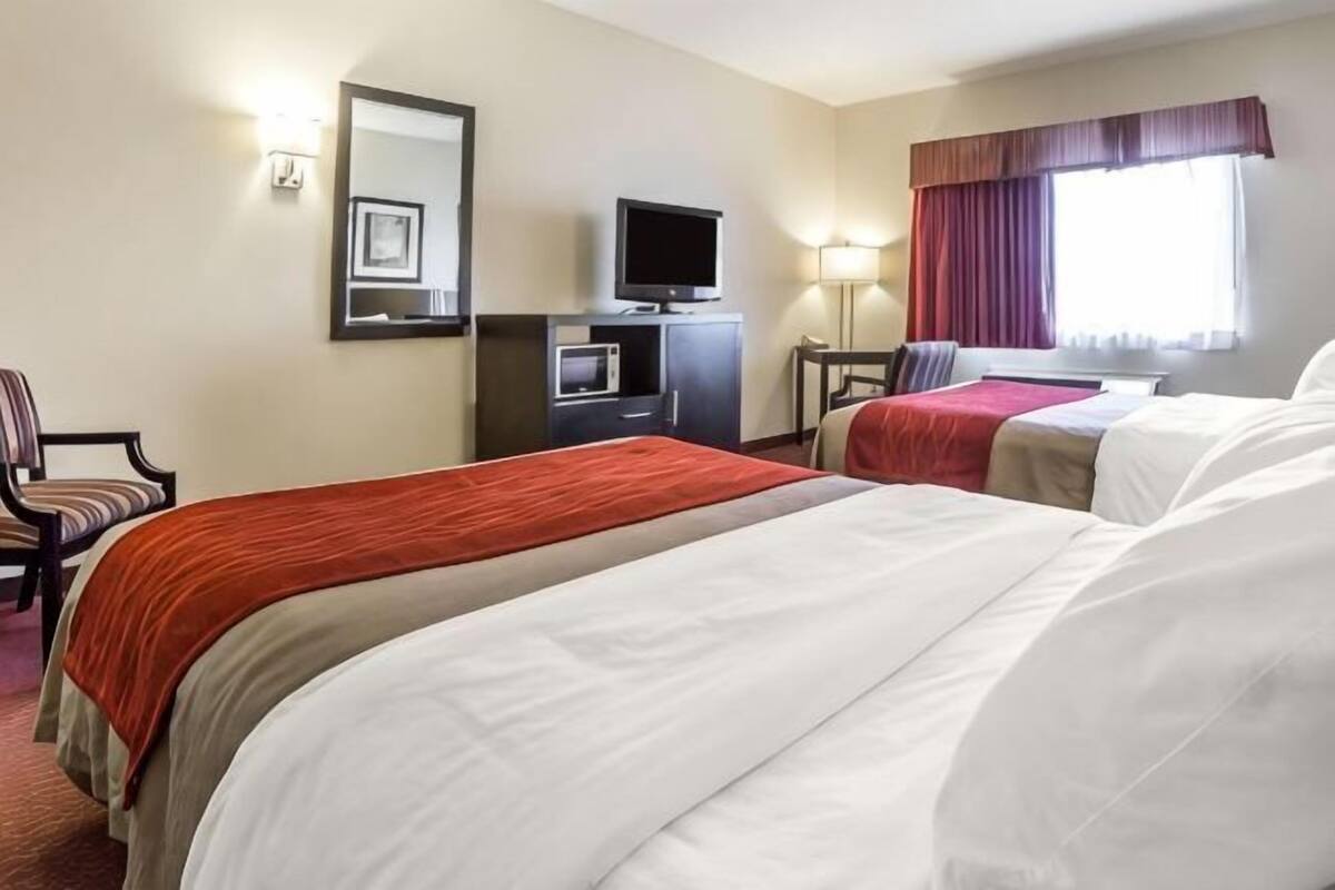 A hotel room with two beds, a desk with a television, a chair, and a window with curtains.