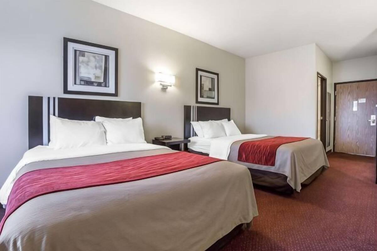 A hotel room with two beds, a nightstand, and a door.