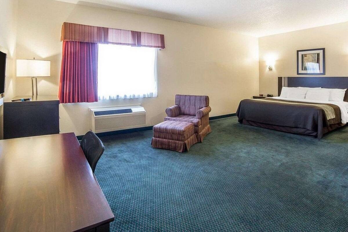 A hotel room with a bed, a desk, a chair, a TV, and a window with curtains.