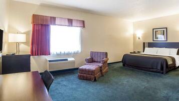 Habitación de hotel con cama, escritorio, silla, televisión y ventana con cortinas.