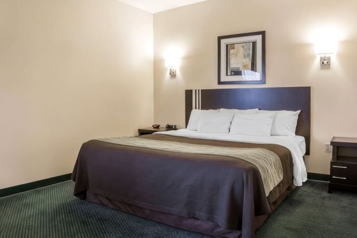 A hotel room with a bed, a nightstand, a framed picture on the wall, and two wall-mounted lights.