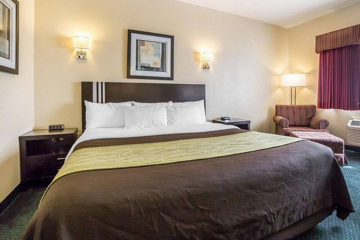 A hotel room with a large bed, two bedside tables, a chair, a desk, and a lamp.