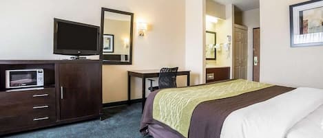 Una habitación de hotel con una cama, un escritorio, un televisor, un microondas y un espejo.