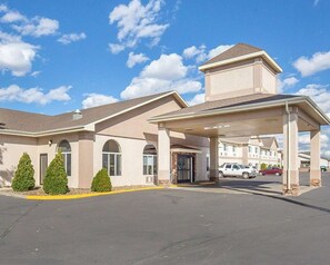 A hotel with a covered entrance, a central tower, and a parking lot.