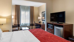 Habitació d'hotel amb un llit, un escriptori, una televisió, un frigorífic i una finestra amb cortines.