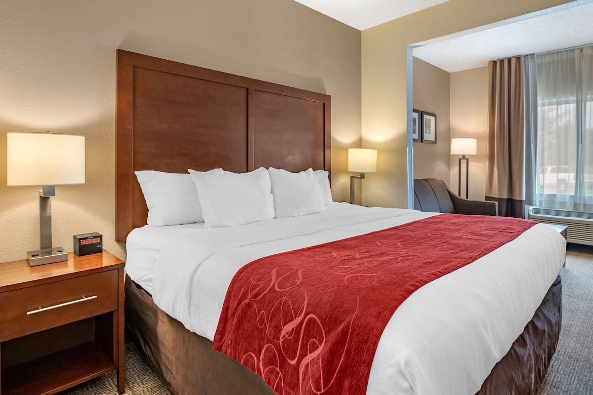 A hotel room with a large bed, two bedside tables with lamps, a chair, and a large window with curtains.