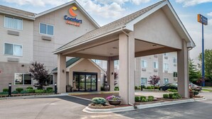 Hotel Comfort Suites amb entrada coberta, aparcament i zones enjardinades amb arbustos i flors.