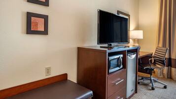 A hotel room with a bed, a desk with a computer, a television, a lamp, and a chair.