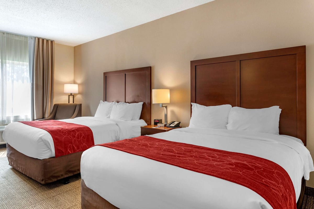 A hotel room with two beds, each with a wooden headboard, white bedding, and a red throw blanket. There are bedside tables with lamps and a telephone.