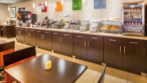 Zona de l'esmorzar d'un hotel modern, amb un sistema de bufet que inclou una màquina de cafè, torradora i diverses opcions de menjar.