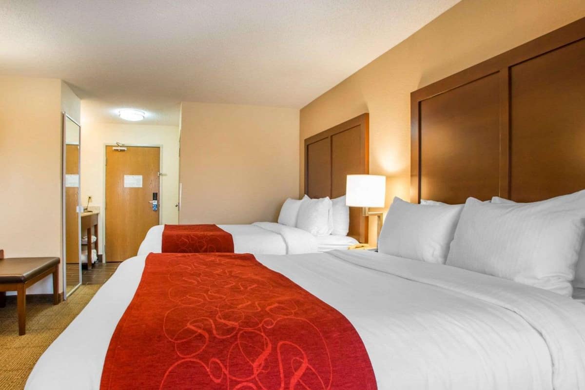 A hotel room with two beds, a desk, and a mirror.
