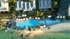 An aerial view of a resort with a large swimming pool, multiple overwater bungalows, and a beach area. - Fisherman’s Cove resort (Mahé Island)