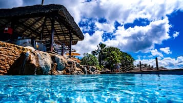 Una piscina con agua cristalina, una construcción con techo de paja y vistas al cielo nublado.