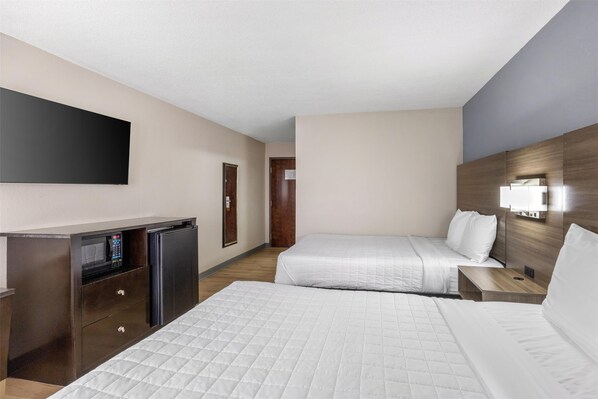 A hotel room with two beds, a desk with a refrigerator, and a flat-screen TV mounted on the wall.