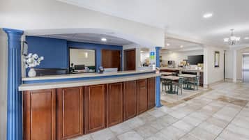 A reception area with a wooden counter, a coffee machine, and a seating area with chairs and a table.