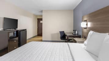A hotel room with a bed, a desk with a chair, a television, a microwave, and a nightstand with a lamp.