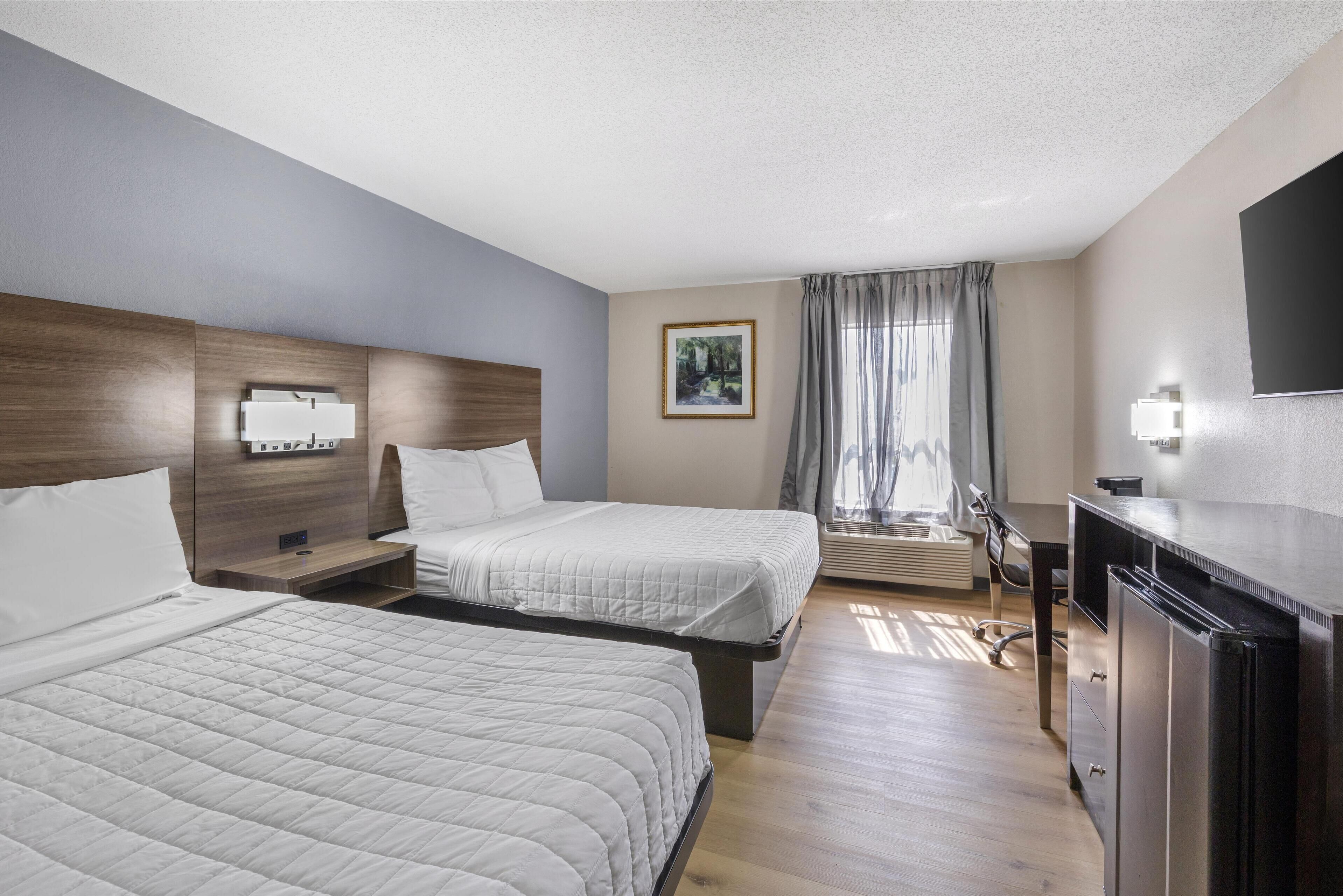 A hotel room with two beds, a desk, a chair, a TV, and a window with curtains.