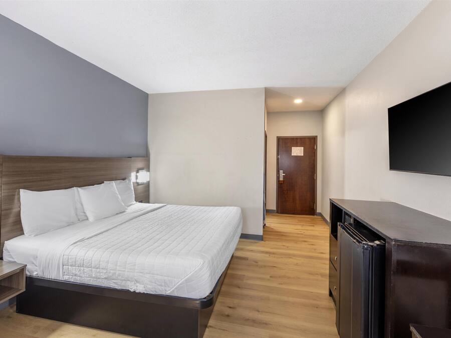 A hotel room with a bed, bedside table, TV, and a wooden cabinet.