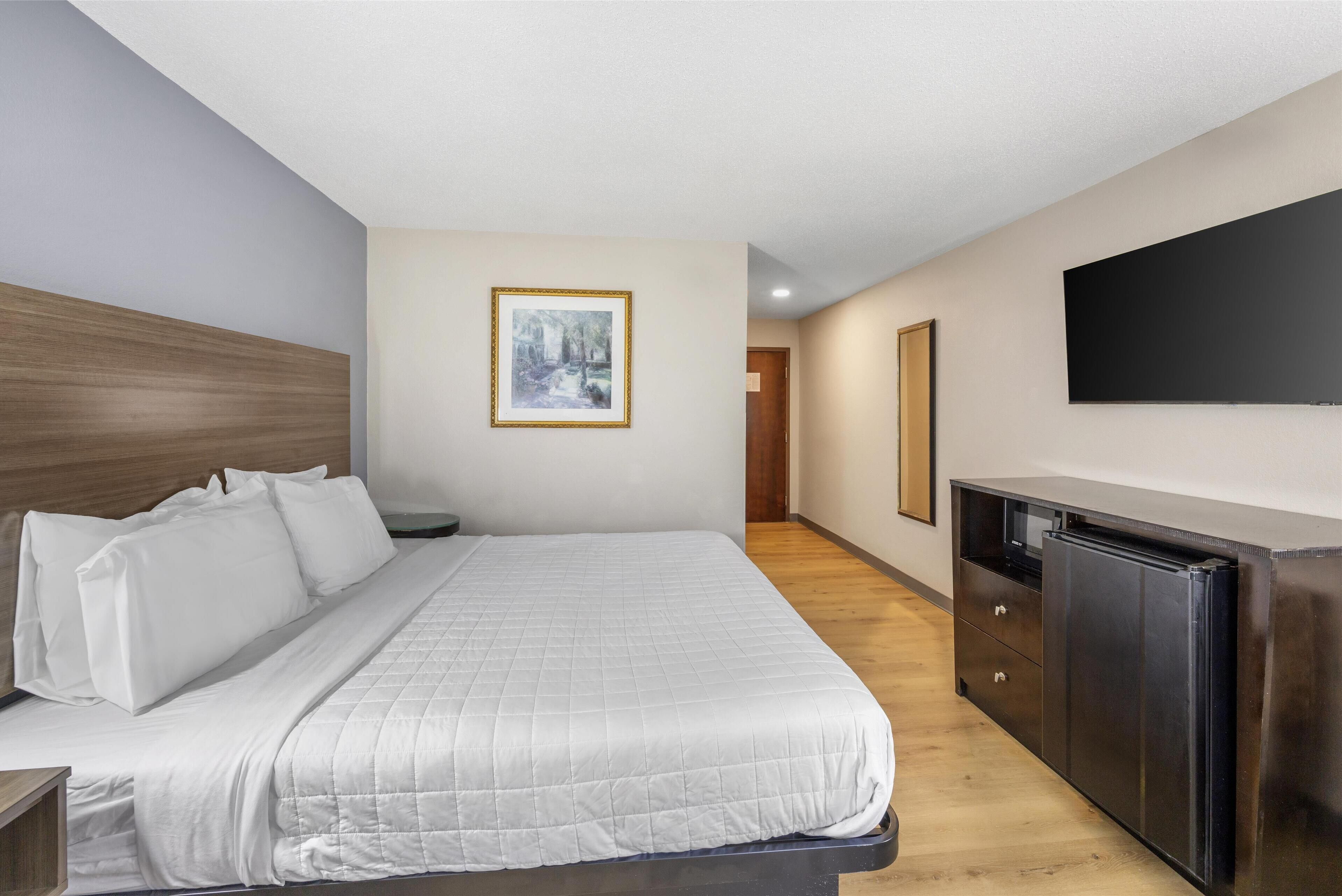 Un cuarto de hotel con una cama grande, cabecera de madera, televisor de pantalla plana, cómoda y un cuadro en la pared.