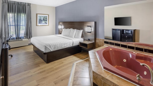 Een hotelkamer met een groot bed, een rode jacuzzi, een flatscreen televisie en een raam met gordijnen.