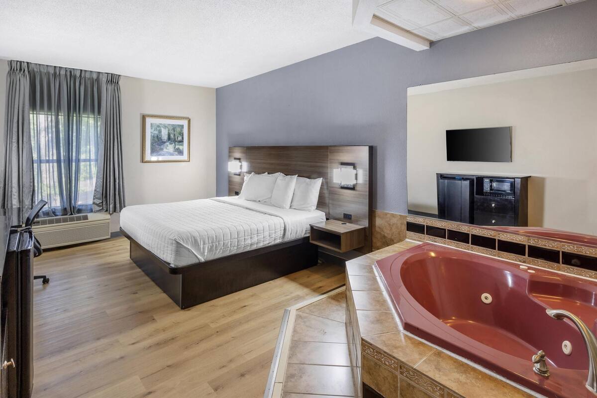 Ein Hotelzimmer mit einem großen Bett, einer roten Whirlwanne, einem Flachbildfernseher und einem fenster mit Vorhängen.
