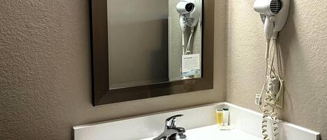 Un baño con lavamanos blanco, un espejo y un secador de pelo montado en la pared.