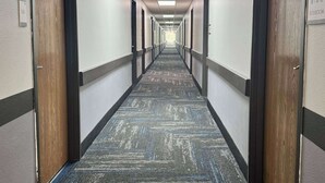 A long, narrow hotel corridor with carpeted floors, wooden doors, and a sign indicating a restroom. - Quality Inn Sulphur - Lake Charles (Sulphur)