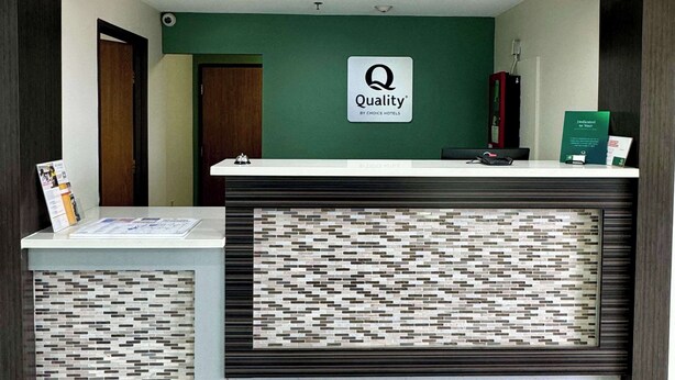 A hotel reception desk with a 'Quality by Choice Hotels' sign, a reception counter, and a patterned wall. - Quality Inn Sulphur - Lake Charles (Sulphur)