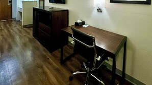 A hotel room with a wooden desk, a chair, a television, a mirror, and a framed picture on the wall. - Quality Inn Sulphur - Lake Charles (Sulphur)
