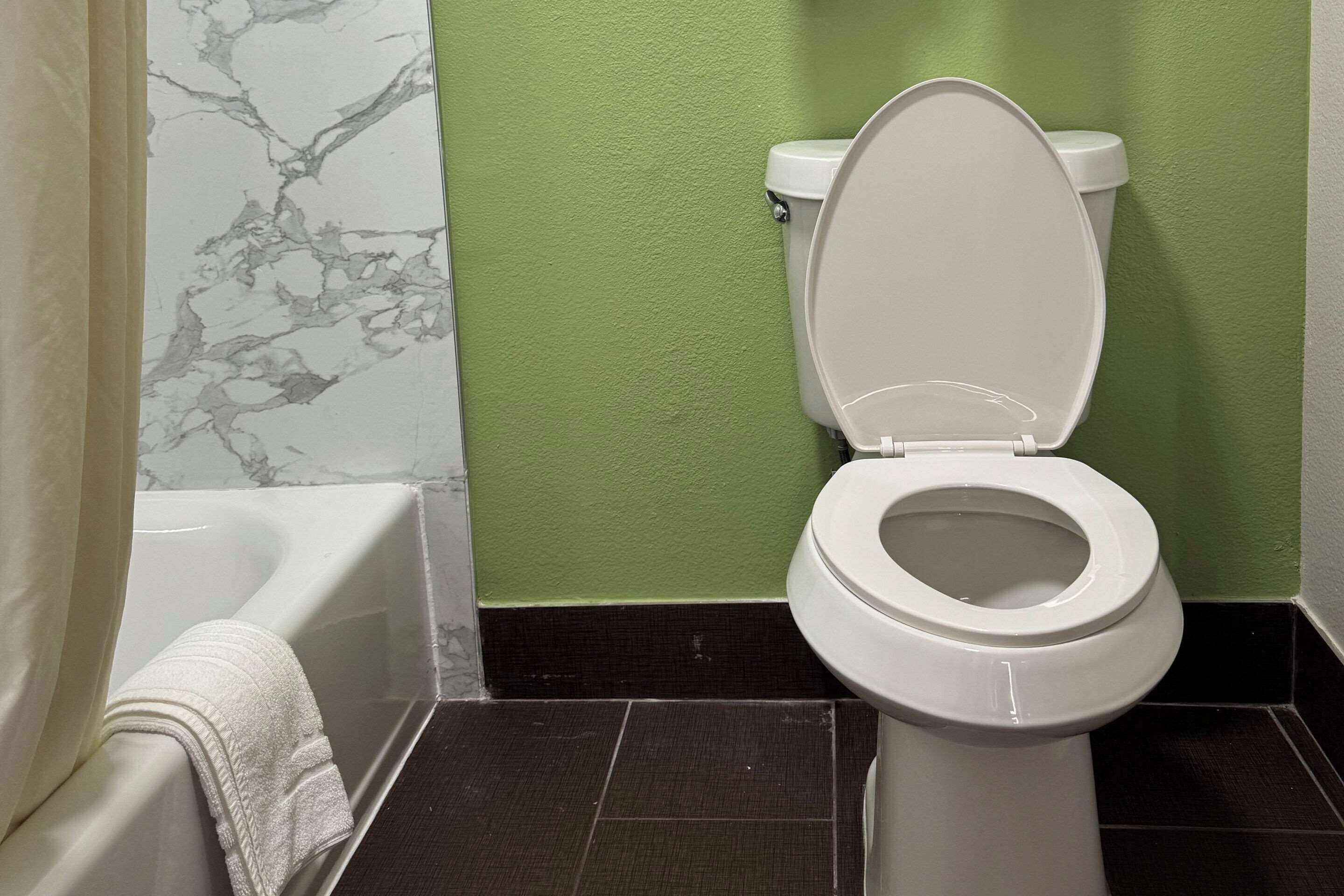 A bathroom with a white toilet, a bathtub, and a green wall.