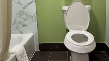 A bathroom with a white toilet, a bathtub, and a green wall.