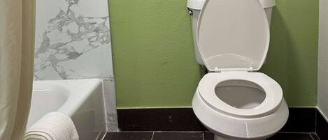 A bathroom with a white toilet, a bathtub, and a green wall.