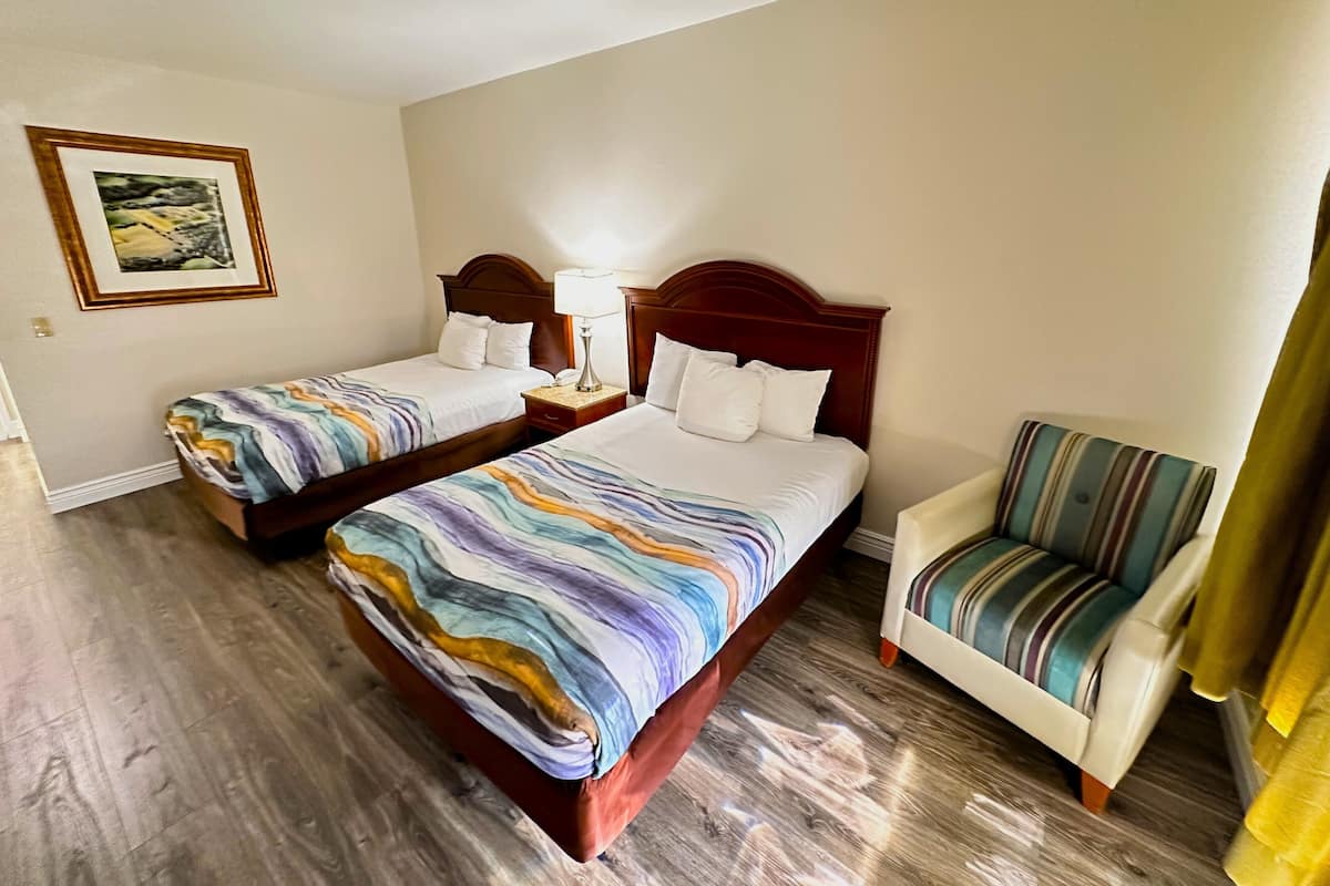 Habitación de hotel con dos camas, una silla, una mesita de noche y un cuadro en la pared.