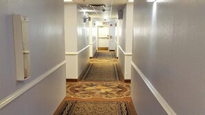 A hotel hallway with a patterned carpet, white walls, and a door at the end.
