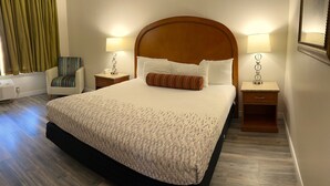 A hotel room with a large bed, two bedside tables with lamps, a chair, and a window with curtains.