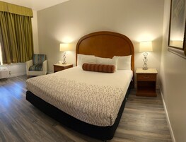 Quarto de hotel com uma cama grande, duas mesas de cabeceira com luminárias, uma cadeira e uma janela com cortinas.