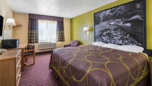 Habitació d'hotel amb un llit gran, una taula de treball amb un ordinador, una cadira, un televisor i una finestra ampla amb cortines.