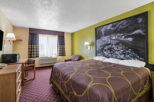 Habitación de hotel con una cama grande, un escritorio con computadora, una silla, un televisor y un ventanal con cortinas.