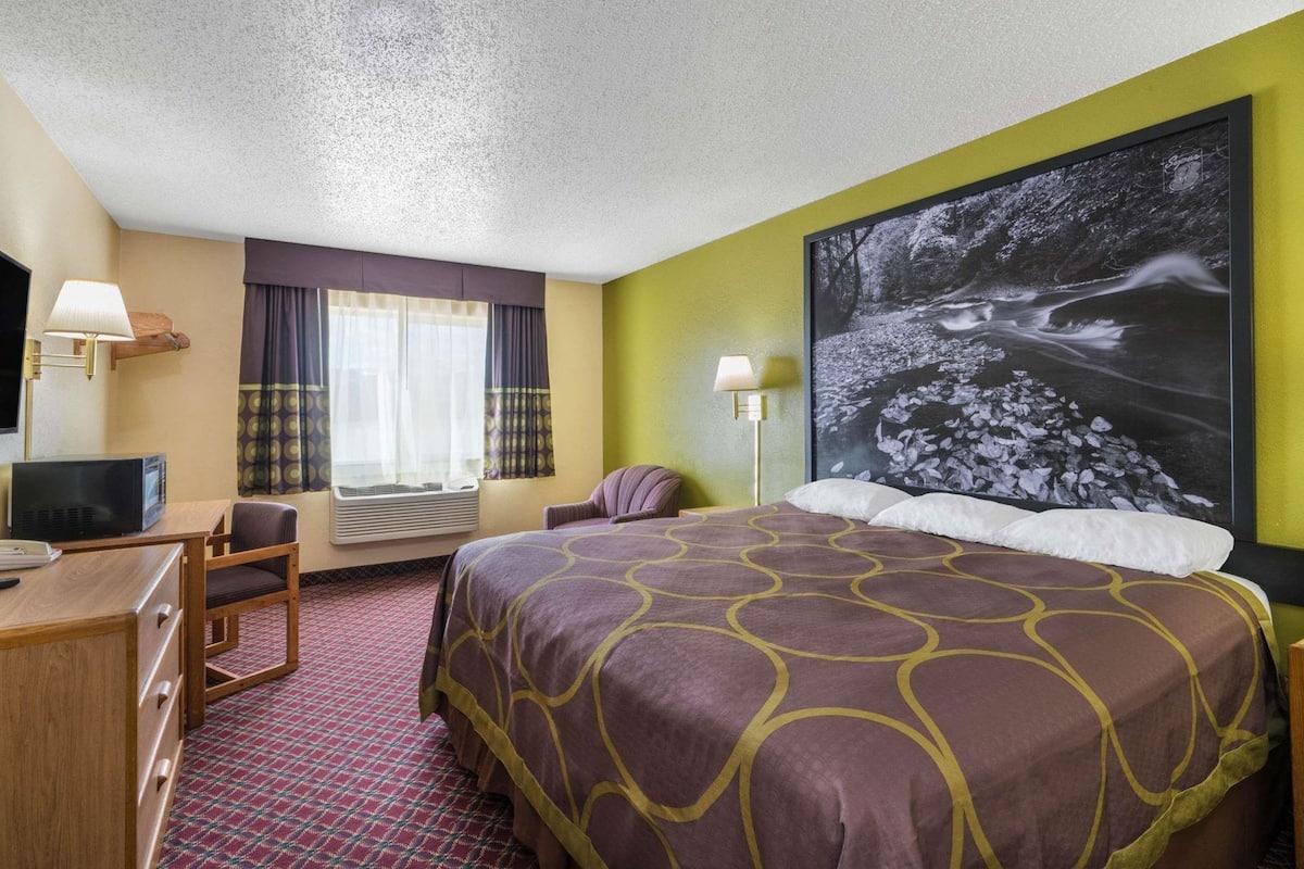 A hotel room with a bed, desk, chair, television, and a large framed picture on the wall.