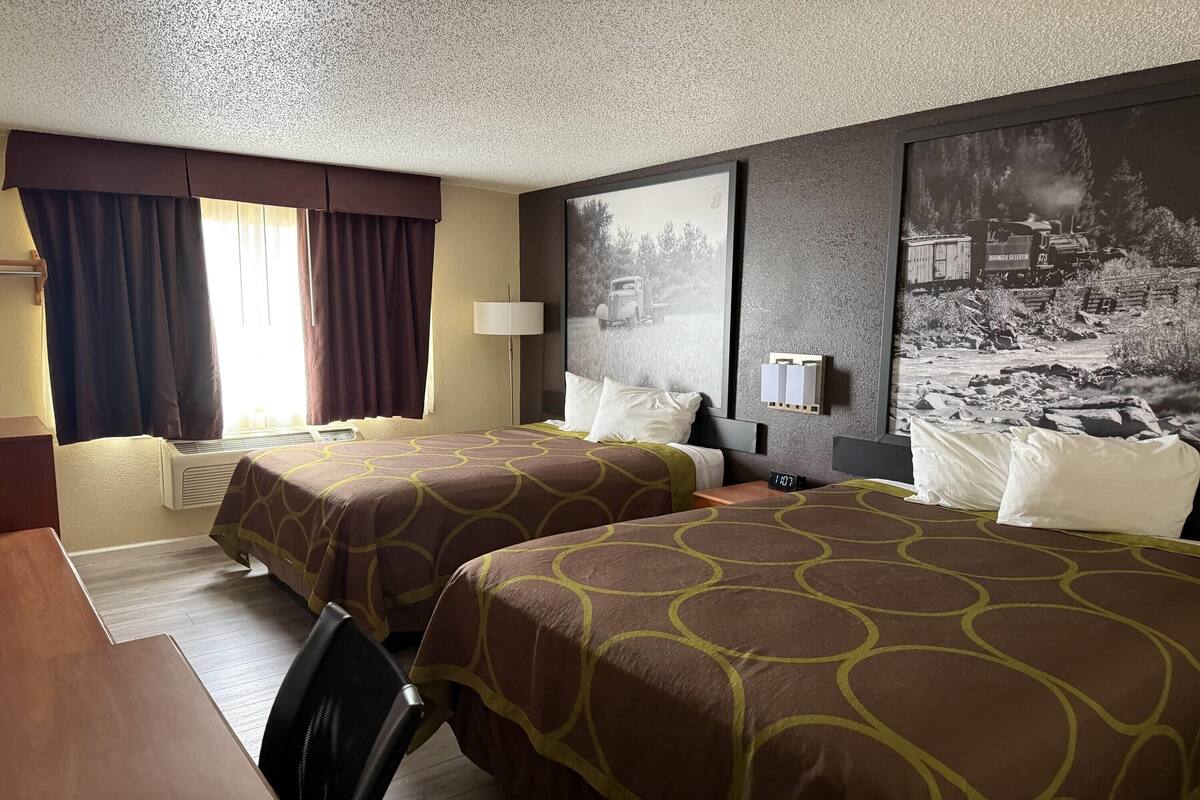 A hotel room with two beds, a desk, a chair, a lamp, and a large framed picture on the wall.