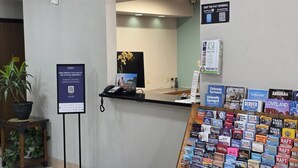 Taulell de recepció d'hotel amb un terminal de pagament, un codi QR per a l'enregistrament automàtic i una presentació de fulletons turístics.