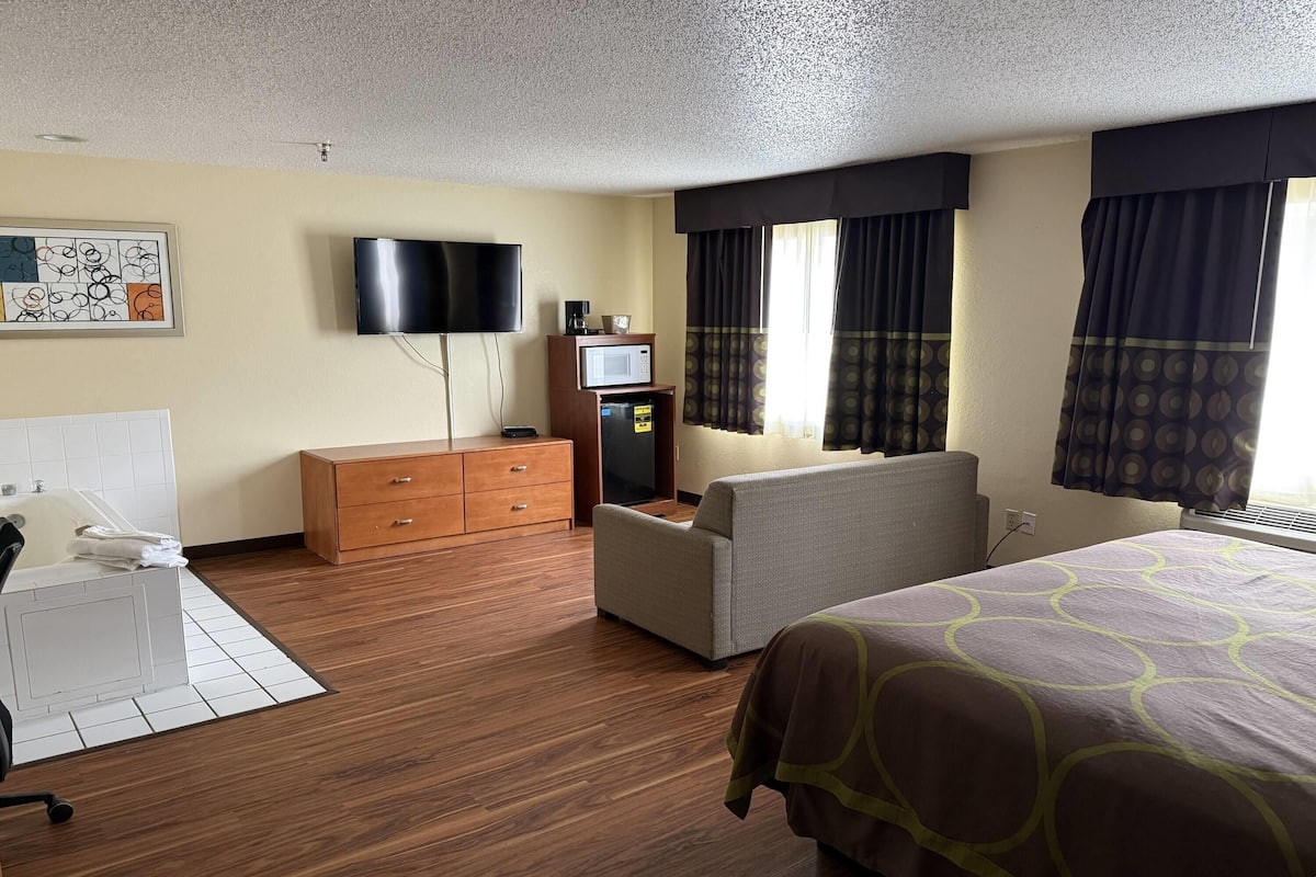 A hotel room with a bed, a sofa, a desk with a chair, a television, a microwave, and a window with curtains.
