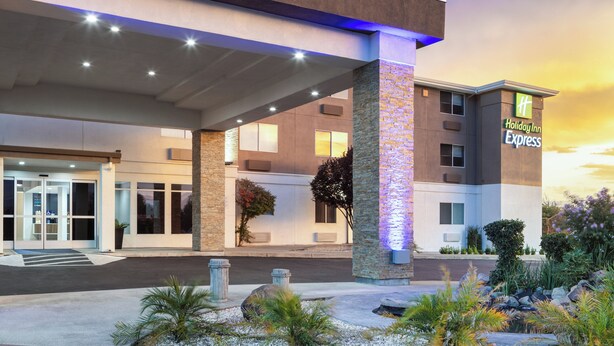 A Holiday Inn Express building with a modern design, featuring a prominent entrance with glass doors, a covered walkway, and a landscaped area with rocks and plants. - Holiday Inn Express Redding North by IHG (Redding)