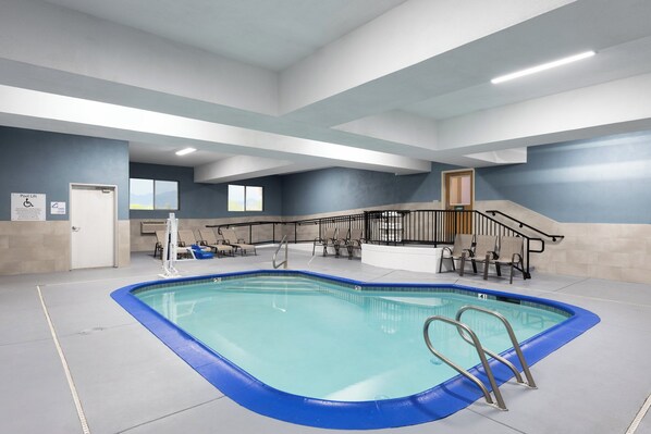 An indoor swimming pool with a blue border, a pool lift, and a staircase with a railing leading to a balcony.