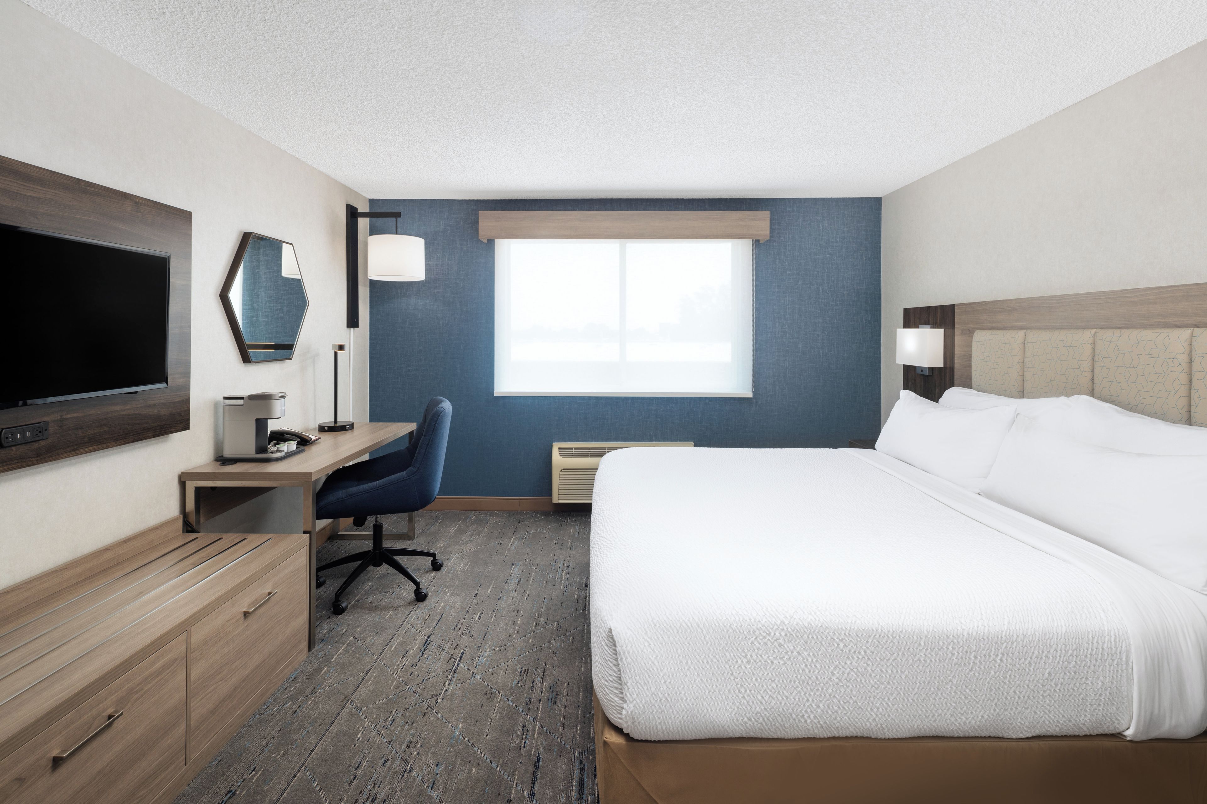 A hotel room with a bed, desk, chair, TV, and a window.