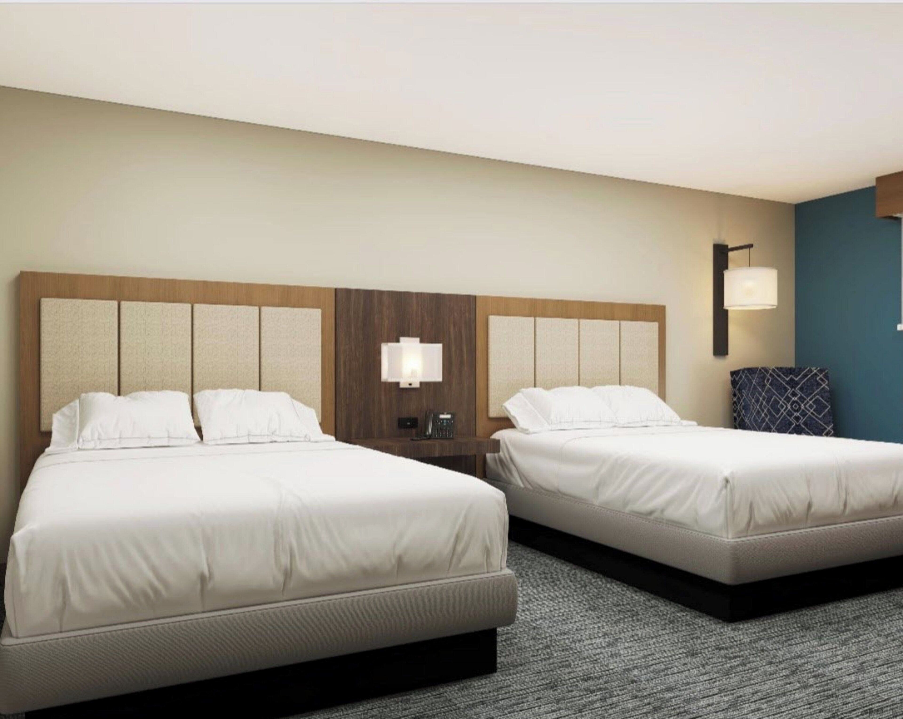 A hotel room with two beds, a nightstand with a lamp, and a blue accent wall.